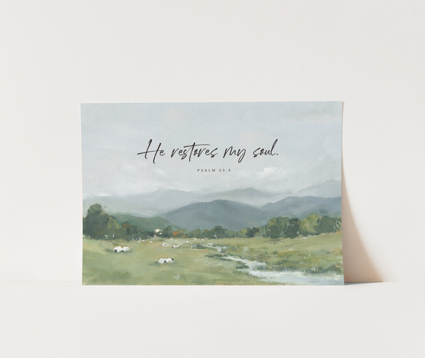 Serene landscape art print of peaceful sheep resting in green pasture with the verse “He restores my soul” from Psalm 23.