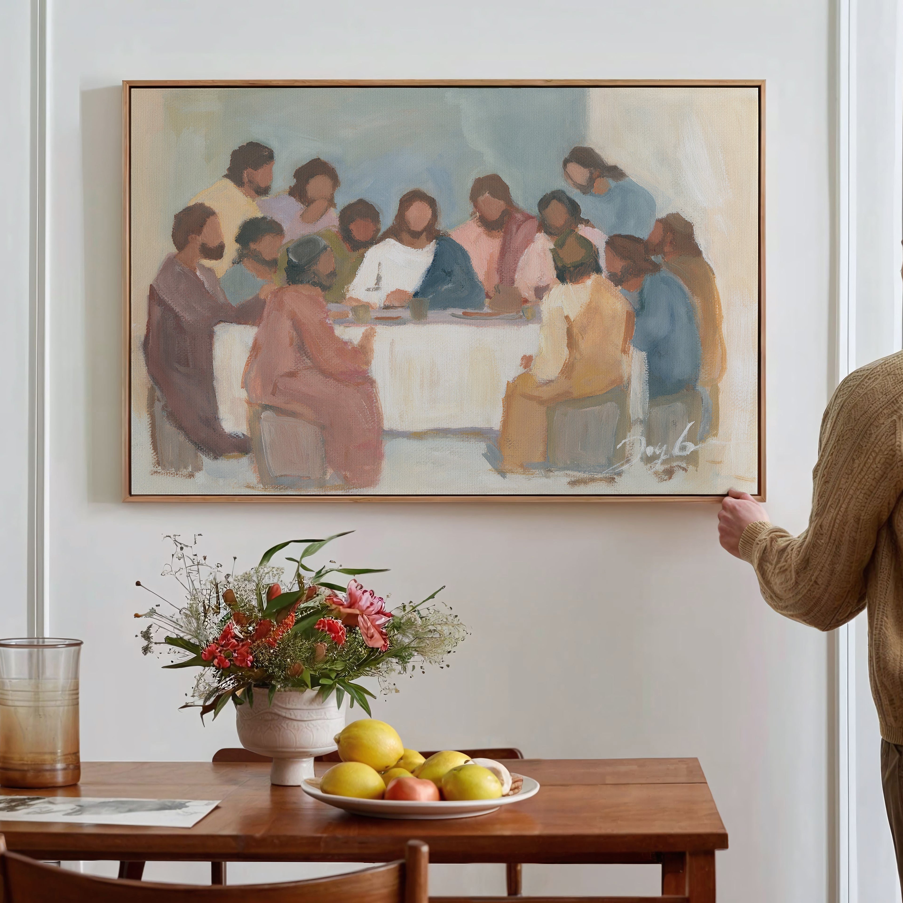 Man standing in a room with a painting of 'The Last Supper' above a wooden table with fruit and flowers.
