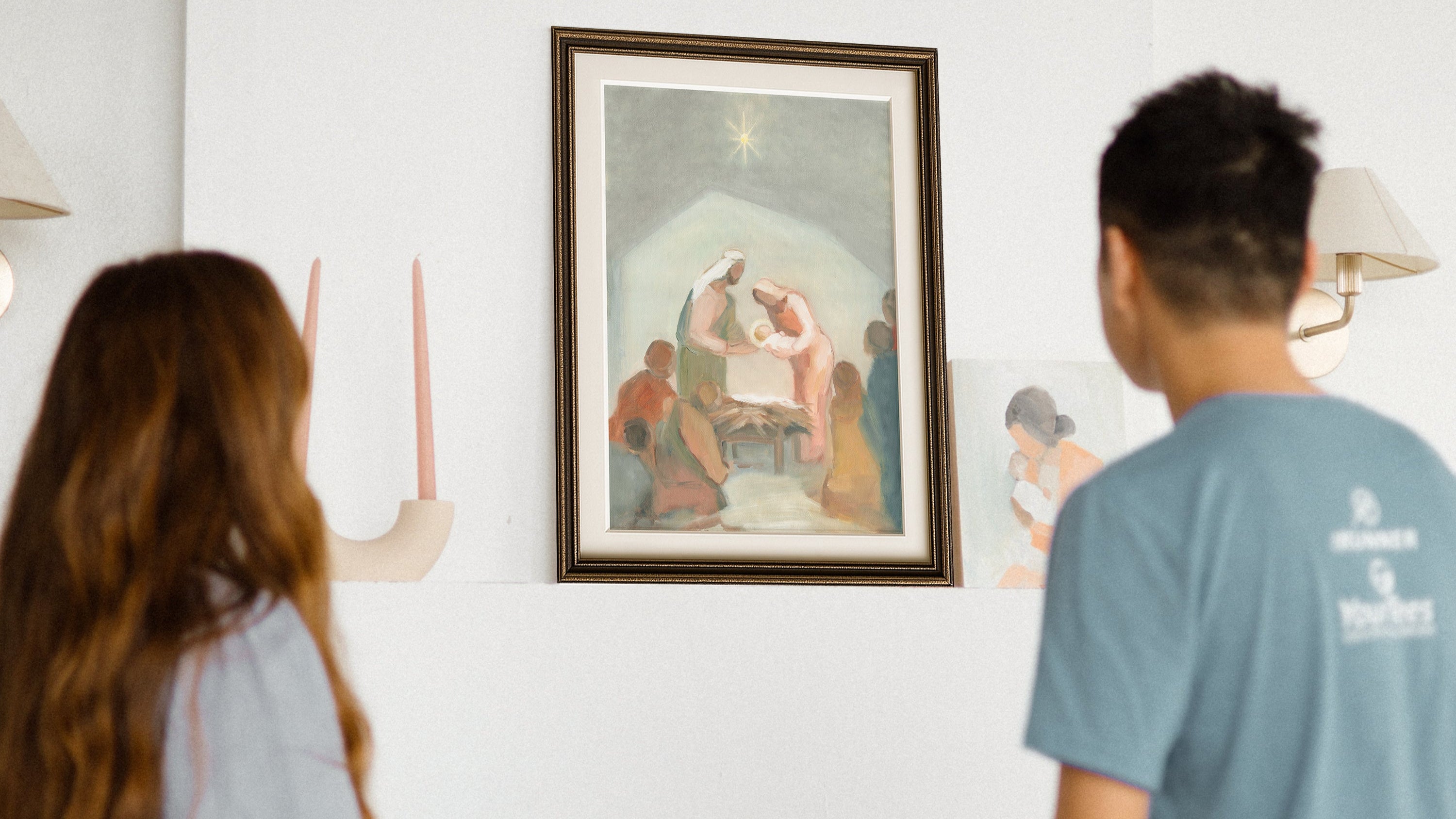 Two people looking at a framed Christian Bible painting of a religious scene on a wall.
